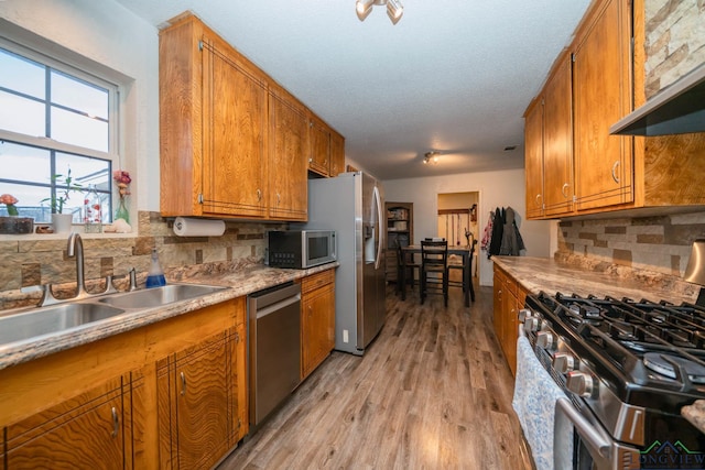 kitchen featuring a textured ceiling, stainless steel appliances, light wood-type flooring, and tasteful backsplash