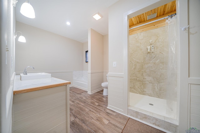 bathroom with hardwood / wood-style floors, vanity, toilet, and tiled shower