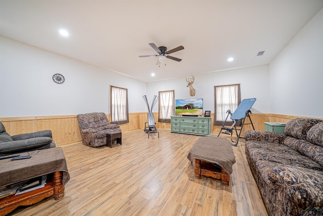 living room with ceiling fan, wood walls, and light hardwood / wood-style flooring