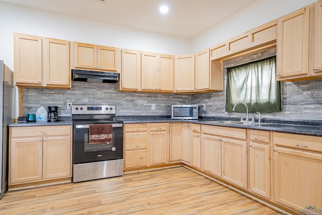 kitchen with light wood-type flooring, appliances with stainless steel finishes, light brown cabinets, and dark stone countertops