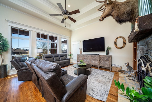 living room with ceiling fan, a fireplace, ornamental molding, wood-type flooring, and a raised ceiling