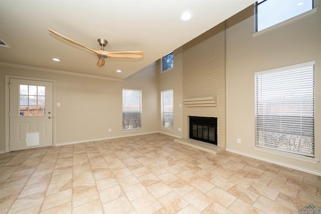 unfurnished living room featuring crown molding, ceiling fan, a brick fireplace, and a towering ceiling