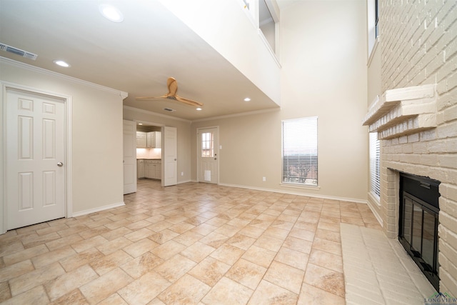 unfurnished living room featuring a high ceiling, ornamental molding, a brick fireplace, and ceiling fan