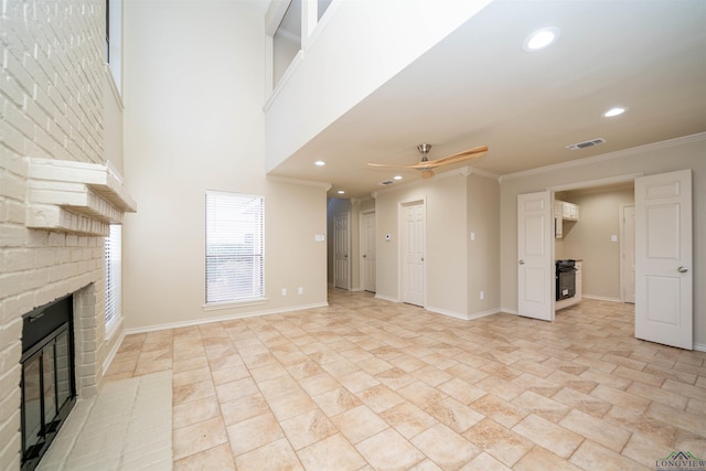 unfurnished living room with a high ceiling, crown molding, ceiling fan, and a fireplace