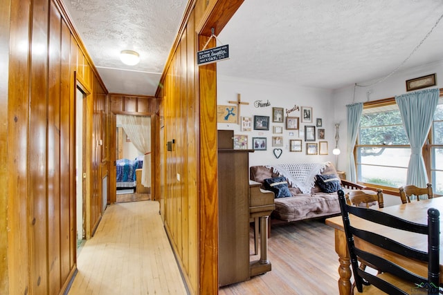 hallway with wooden walls, light hardwood / wood-style flooring, and a textured ceiling