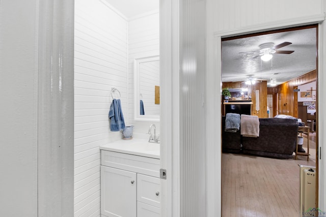 bathroom featuring wood walls, a textured ceiling, vanity, hardwood / wood-style flooring, and ceiling fan