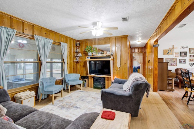 living room featuring crown molding, ceiling fan, light hardwood / wood-style floors, a textured ceiling, and wood walls