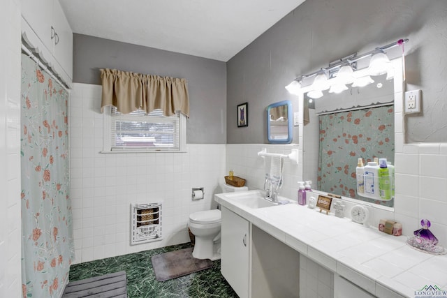 bathroom featuring heating unit, vanity, toilet, and tile walls