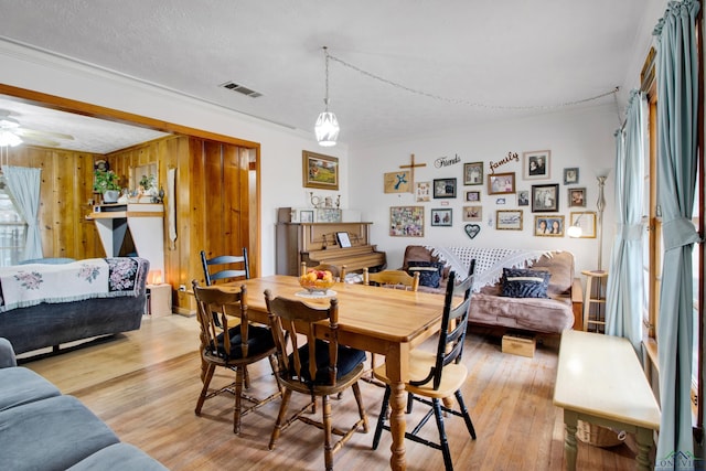 dining space with wood walls, ornamental molding, ceiling fan, a textured ceiling, and light hardwood / wood-style flooring