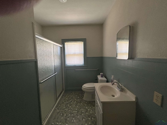 bathroom with wainscoting, toilet, vanity, a shower stall, and tile walls