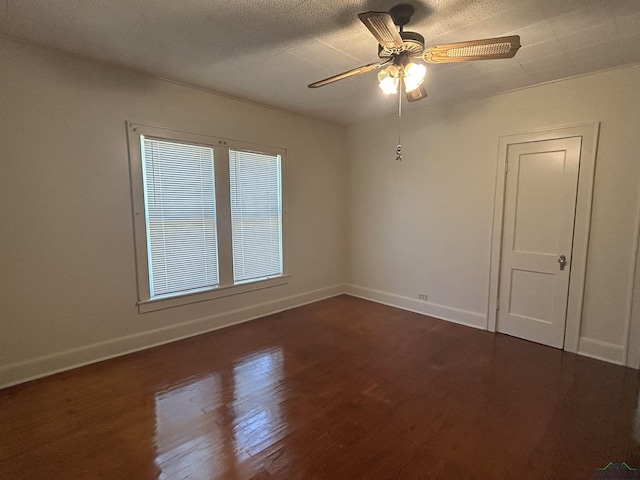 unfurnished room with dark wood-style floors, a ceiling fan, and baseboards