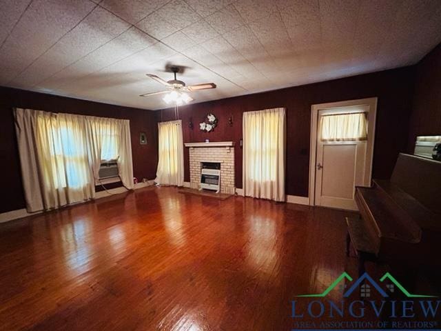 unfurnished living room with a brick fireplace, ceiling fan, baseboards, and wood finished floors