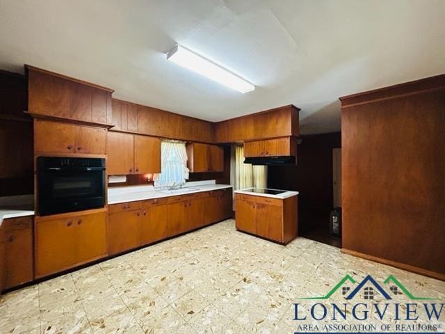 kitchen featuring light floors, light countertops, brown cabinetry, a sink, and black appliances