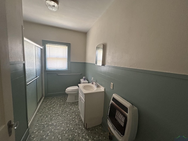 bathroom featuring heating unit, toilet, wainscoting, a shower stall, and vanity