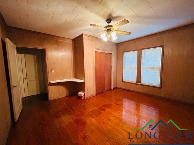 unfurnished bedroom featuring ceiling fan, wood walls, and hardwood / wood-style flooring