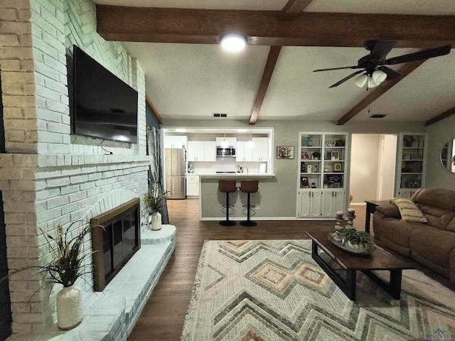 1101 N Idlewood Dr, White Oak, TX 75693 - living area featuring beamed ceiling, dark wood-style floors, a fireplace, ceiling fan, and a textured ceiling