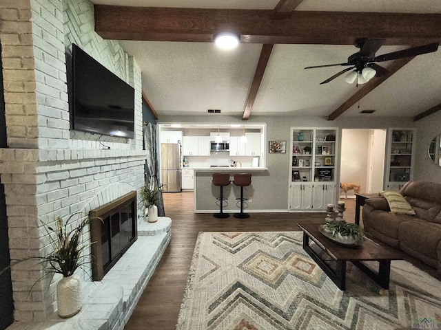 1101 N Idlewood Dr, White Oak, TX 75693 - living room with a fireplace, beamed ceiling, dark wood finished floors, a ceiling fan, and a textured ceiling