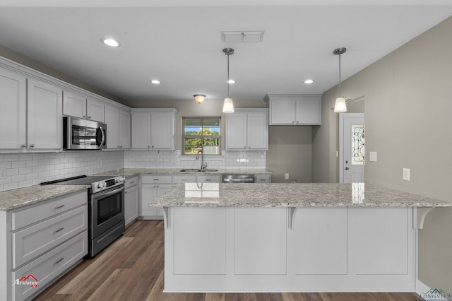 kitchen with light stone countertops, sink, kitchen peninsula, decorative light fixtures, and appliances with stainless steel finishes