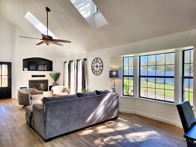 living room with a water view, a skylight, ceiling fan, a fireplace, and wood-type flooring