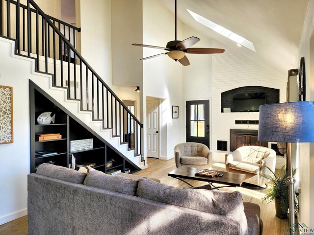 living room with a skylight, ceiling fan, wood-type flooring, and a high ceiling