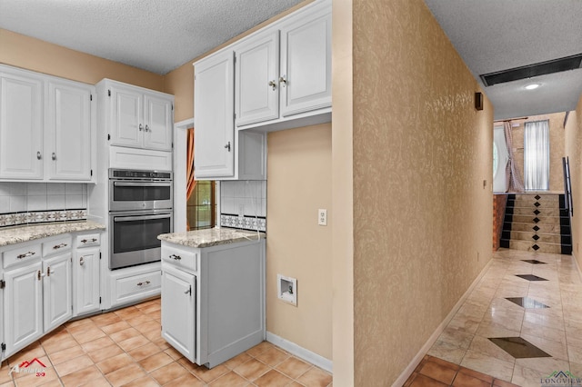 1502 Meandering Way, Longview, TX 75604 - kitchen featuring stainless steel double oven, a textured ceiling, white cabinets, backsplash, and light stone countertops