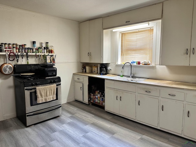 kitchen with stainless steel gas stove, light hardwood / wood-style floors, white cabinetry, and sink