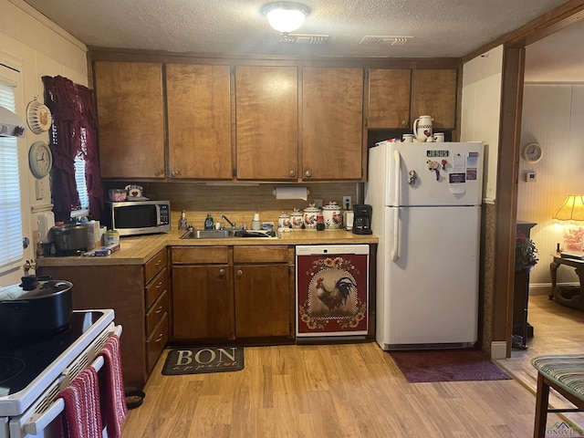 kitchen with sink, white appliances, light hardwood / wood-style flooring, and a textured ceiling