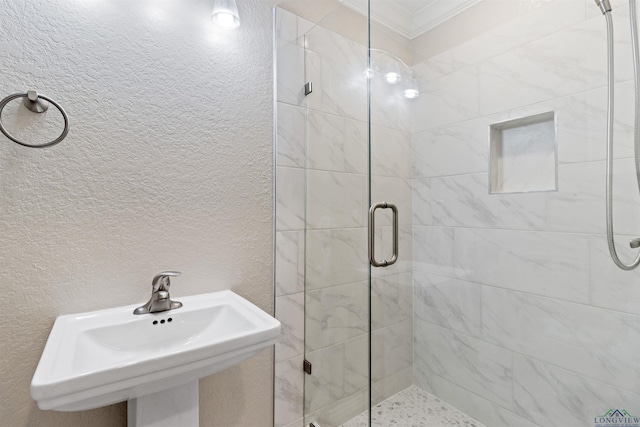 bathroom featuring a shower with shower door, crown molding, and sink