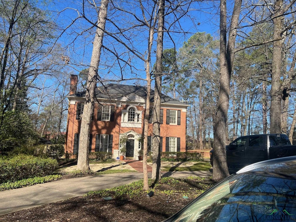 colonial inspired home with brick siding and a chimney