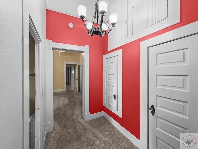 hallway with dark colored carpet and a chandelier