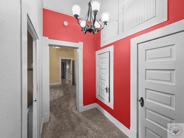 hallway with dark colored carpet and a chandelier