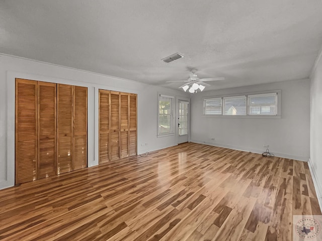 unfurnished bedroom with ceiling fan, two closets, a textured ceiling, and hardwood / wood-style flooring