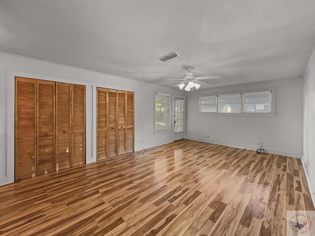 unfurnished bedroom with ceiling fan, two closets, a textured ceiling, and hardwood / wood-style flooring