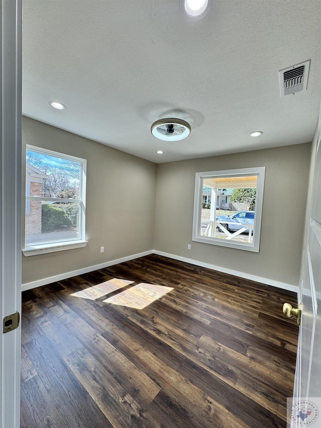 spare room featuring dark wood-type flooring, plenty of natural light, visible vents, and baseboards