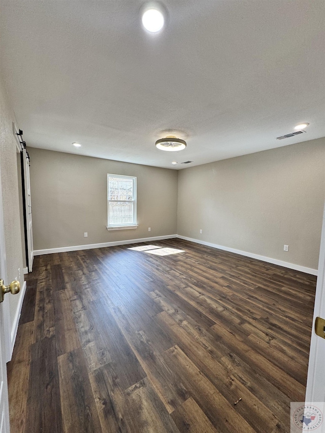 empty room featuring a barn door, visible vents, baseboards, dark wood-style flooring, and a textured ceiling