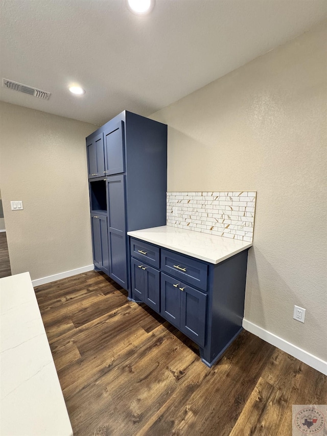 kitchen with dark wood-type flooring, visible vents, baseboards, blue cabinetry, and tasteful backsplash