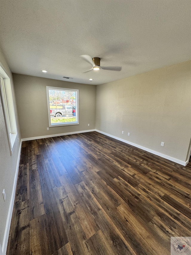 empty room with a textured ceiling, dark wood finished floors, visible vents, and baseboards