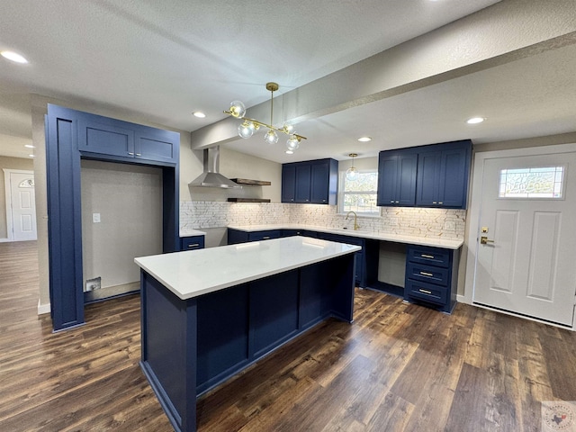 kitchen featuring blue cabinetry, a center island, wall chimney exhaust hood, tasteful backsplash, and dark wood finished floors