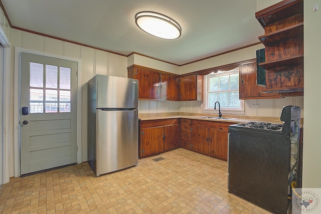 kitchen featuring sink, black range with gas cooktop, ornamental molding, and stainless steel fridge