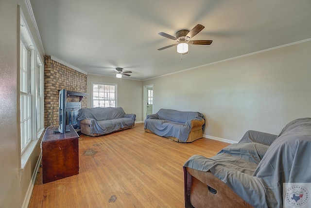 living room featuring ceiling fan, light wood-type flooring, a brick fireplace, and ornamental molding