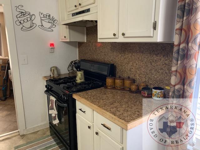 3812 Elizabeth St, Texarkana, TX 75501 - kitchen with black gas range oven, under cabinet range hood, tasteful backsplash, white cabinets, and light tile patterned floors