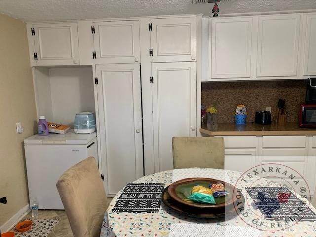 3812 Elizabeth St, Texarkana, TX 75501 - kitchen with fridge, white cabinets, black microwave, decorative backsplash, and a textured ceiling