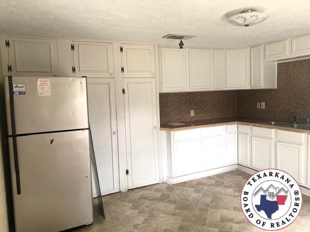 3812 Elizabeth St, Texarkana, TX 75501 - kitchen featuring freestanding refrigerator, a sink, tasteful backsplash, white cabinetry, and a textured ceiling
