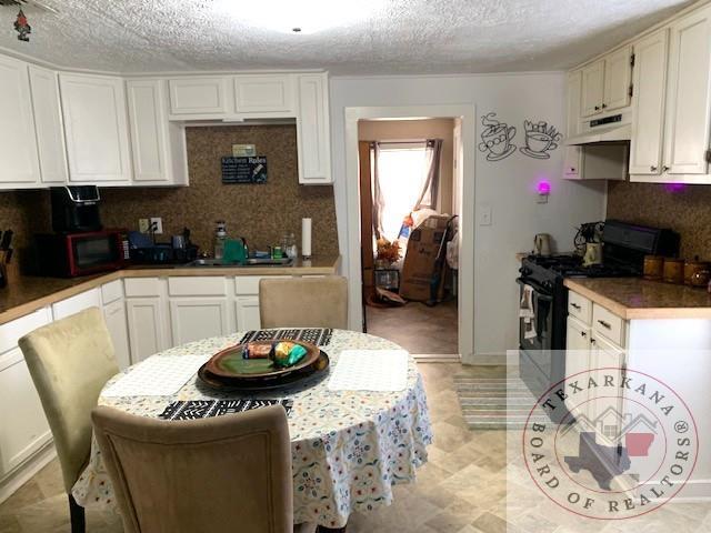3812 Elizabeth St, Texarkana, TX 75501 - kitchen featuring black appliances, white cabinets, tasteful backsplash, a textured ceiling, and under cabinet range hood