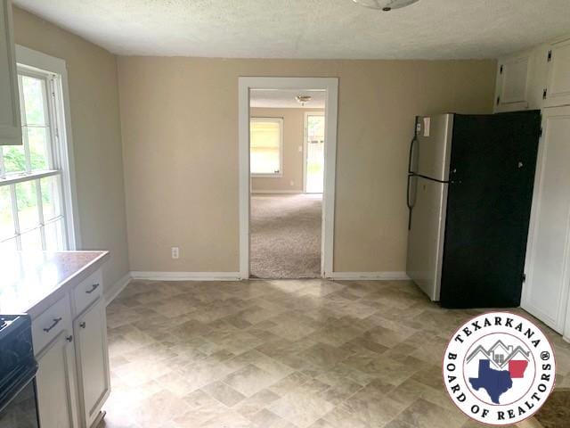 3812 Elizabeth St, Texarkana, TX 75501 - kitchen featuring freestanding refrigerator, healthy amount of natural light, white cabinetry, baseboards, and a textured ceiling