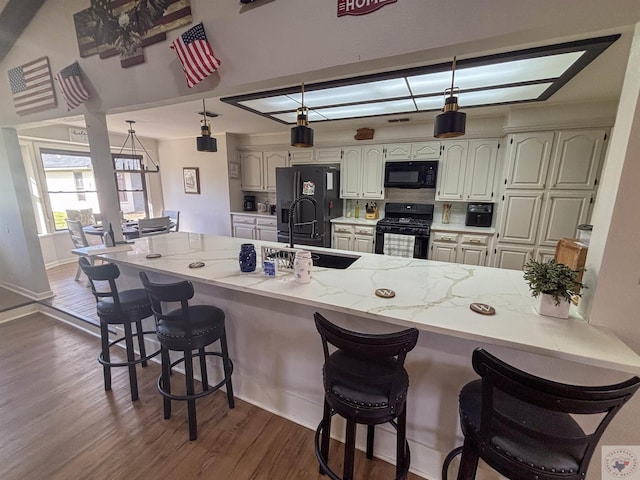 111 Oak St, New Boston, TX 75570 - kitchen with a kitchen bar, dark wood-style flooring, a sink, a peninsula, and black appliances