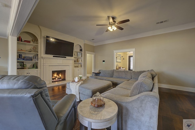 living room with built in shelves, a fireplace, ceiling fan, and ornamental molding