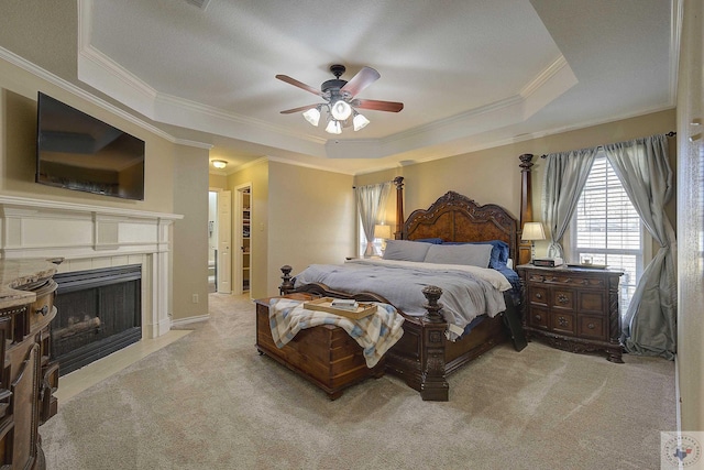 bedroom with crown molding, a tile fireplace, light carpet, ceiling fan, and a tray ceiling