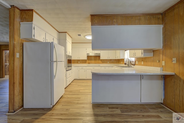 kitchen featuring oven, a sink, under cabinet range hood, freestanding refrigerator, and a peninsula