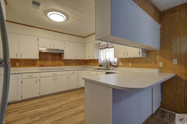 kitchen featuring light countertops, white cabinets, a peninsula, and under cabinet range hood